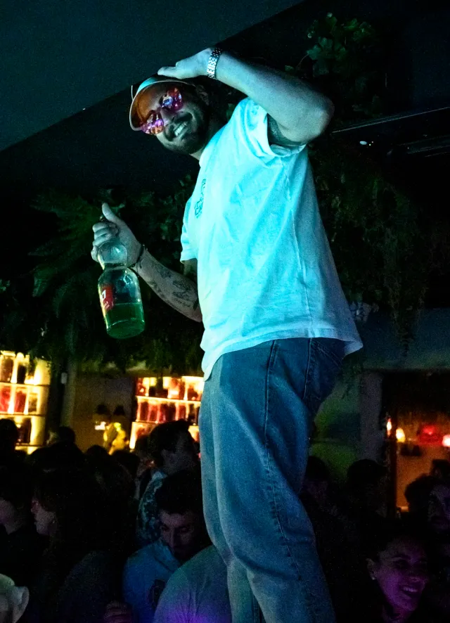 Homme debout sur le bar, une bouteille de Get27 a la main